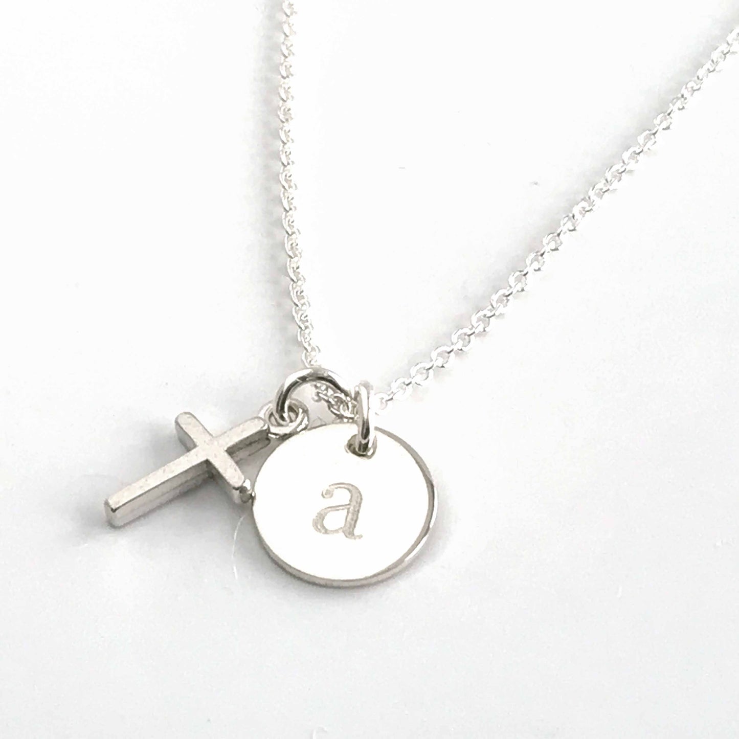 close up of tiny sterling silver cross and engraved initial disc