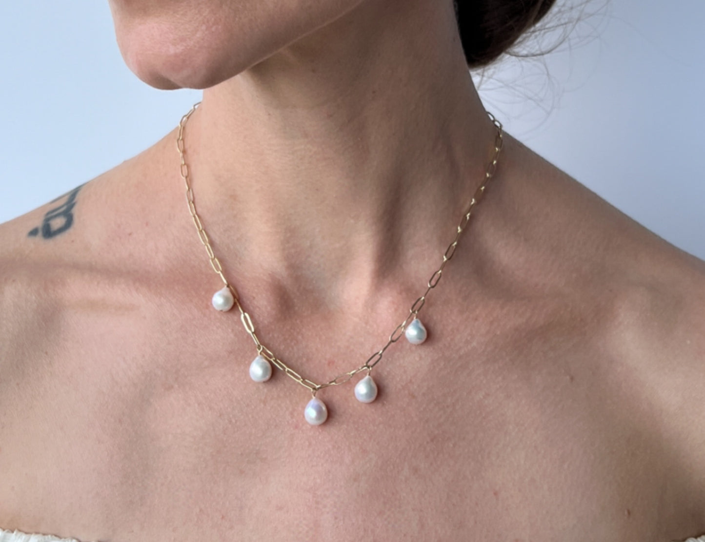 close up of model wearing dangling pearl necklace with baroque pearls and paper clip chain