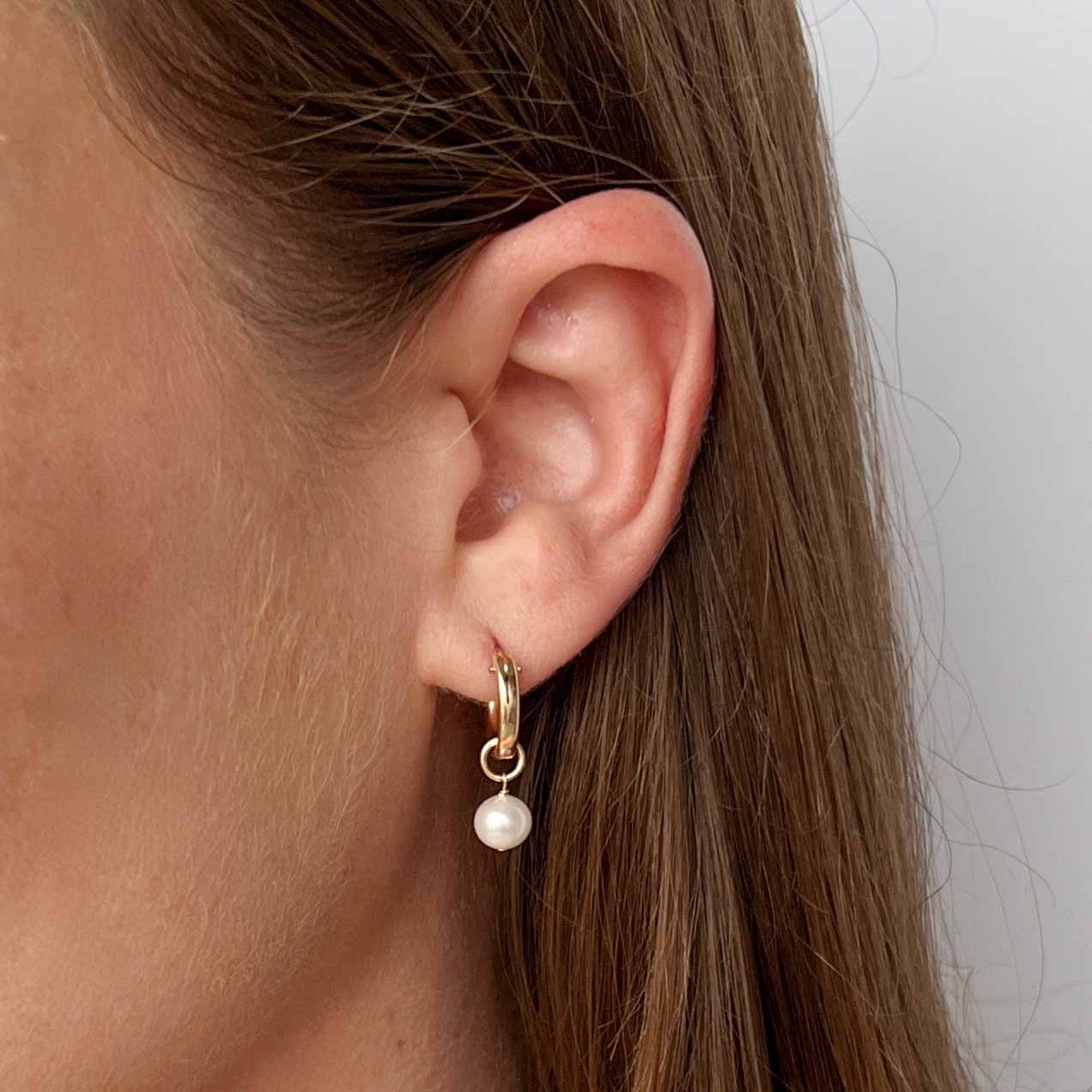 close up of model wearing Lucia pearl huggie earrings in 14k gold filled