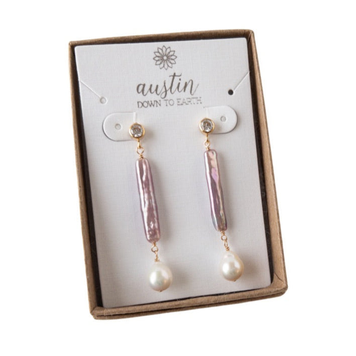 Pair of earrings in a 'Austin Down to Earth' branded box on a white background
