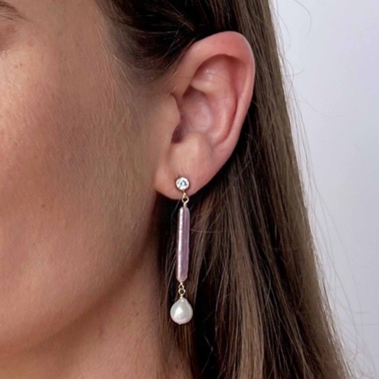 close up of model wearing Vivara CZ Stud Pearl Dangle Earrings with a purple-ish biwa stick pearl and a small baroque pearl