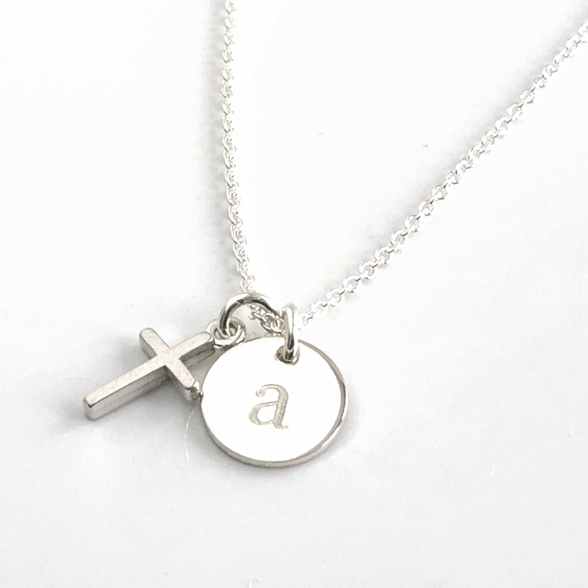close up of tiny sterling silver cross and engraved initial disc