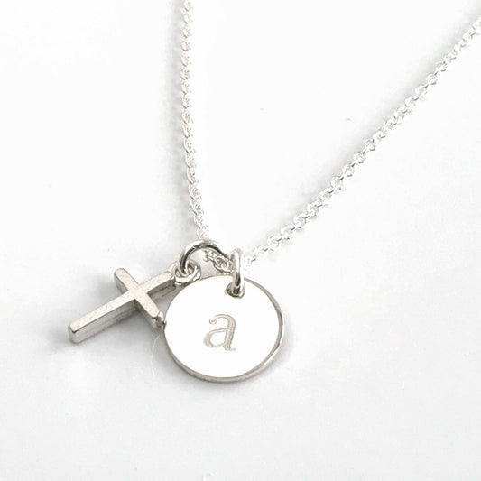 close up of tiny sterling silver cross and engraved initial disc