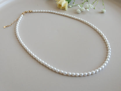 Pearl necklace on a light gray surface with small flowers in the background