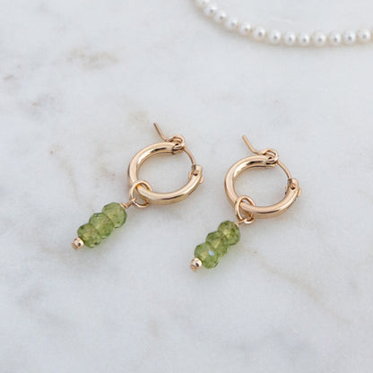 August birthstone peridot gemstone huiggie hoop earrings on marble background