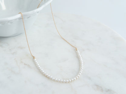 Pearl necklace on a marble surface with a white bowl in the background