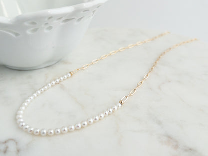 white pearl row draped in front of long pearl necklace with gold paperclip chain