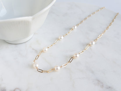 Gold paperclip chain necklace with freshwater pearls on marble surface