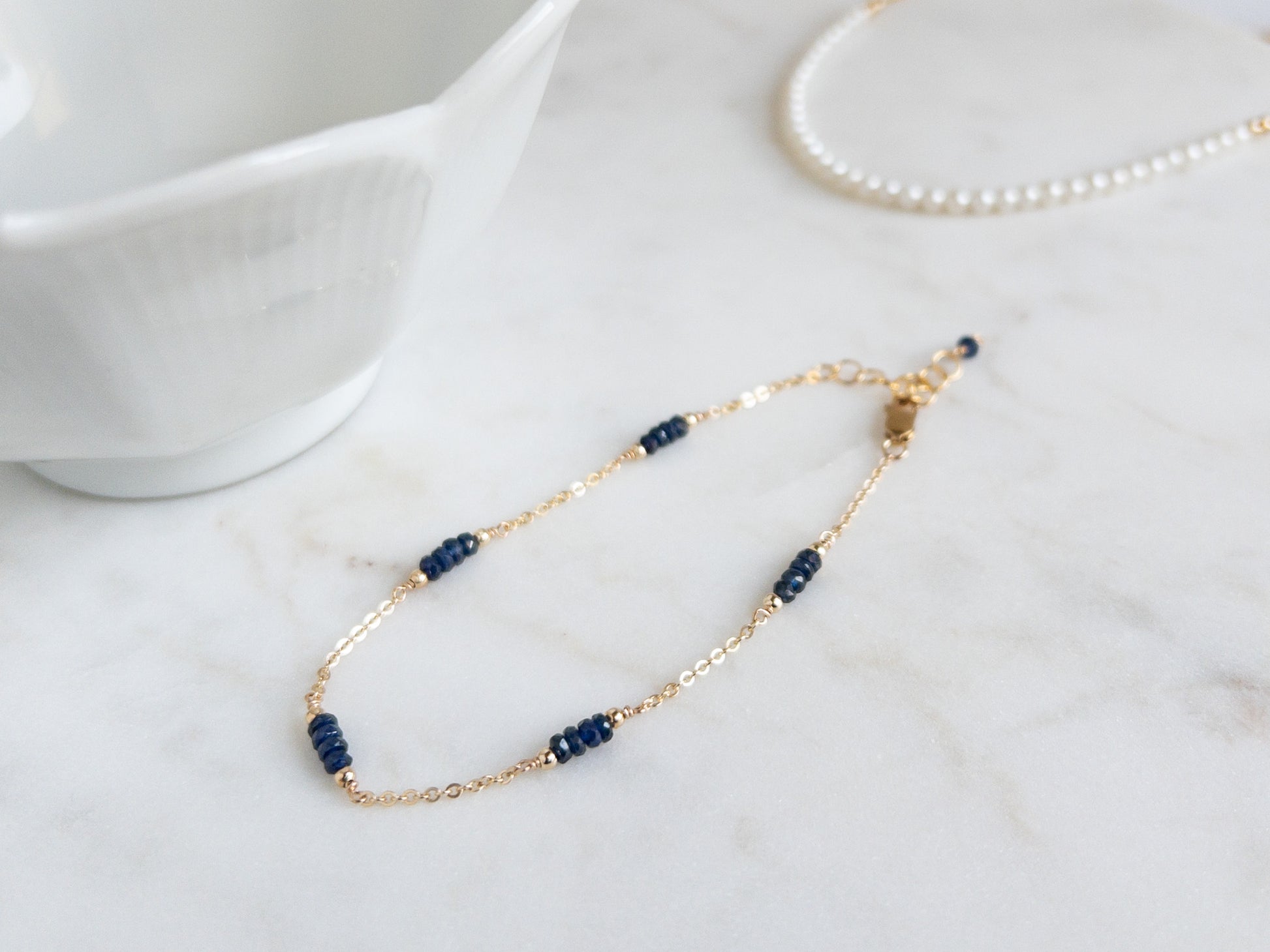 Gold Chain Bracelet with tiny sapphires spaced evenly on chain on marble background