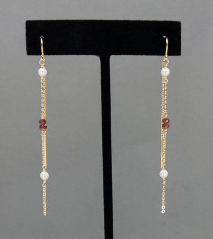 14k gold filled threader earrings with tiny garnets and pearls hanging on an earring stand