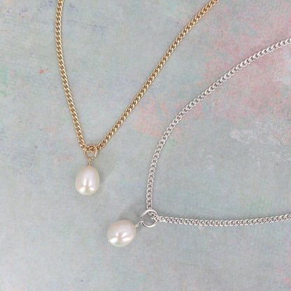 A gold-filled curb chain necklace with freshwater pearl charms, one with a gold chain and one with a silver chain, on a textured background.