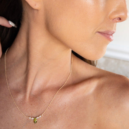 A close-up lifestyle shot of a woman wearing a delicate gold chain necklace with a small green bead and white pearl accent.