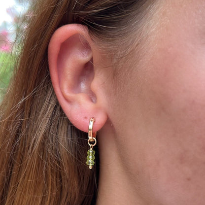 close up of model ear wearing 14k gold filled hoop earrings with peridot gemstone dangles