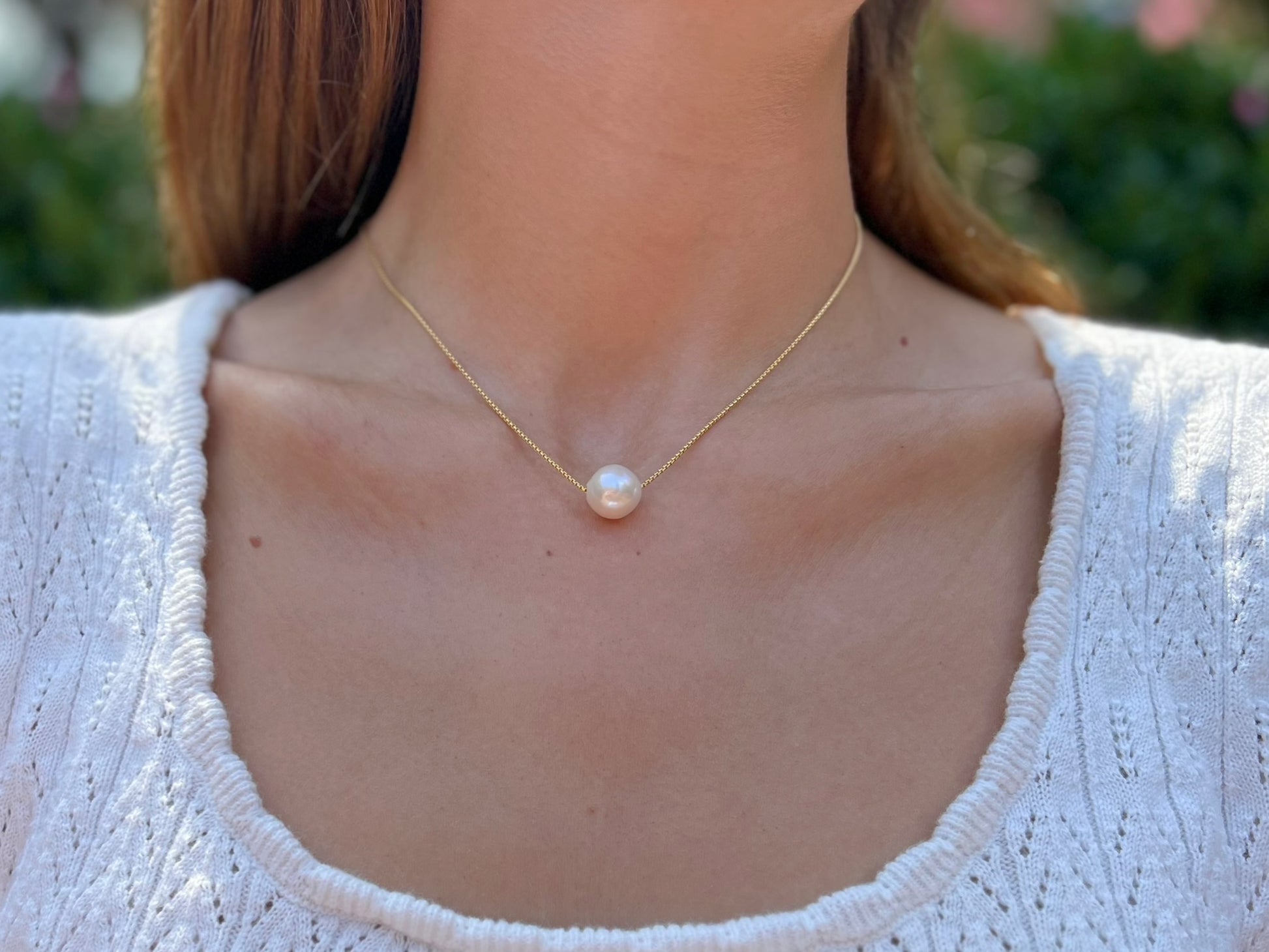 close up of model wearing large floating  pearl necklace.  Pearl is a semi-round white 12mm freshwater pearl 