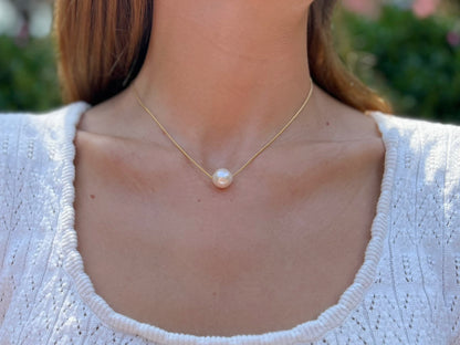 close up of model wearing large floating  pearl necklace.  Pearl is a semi-round white 12mm freshwater pearl 