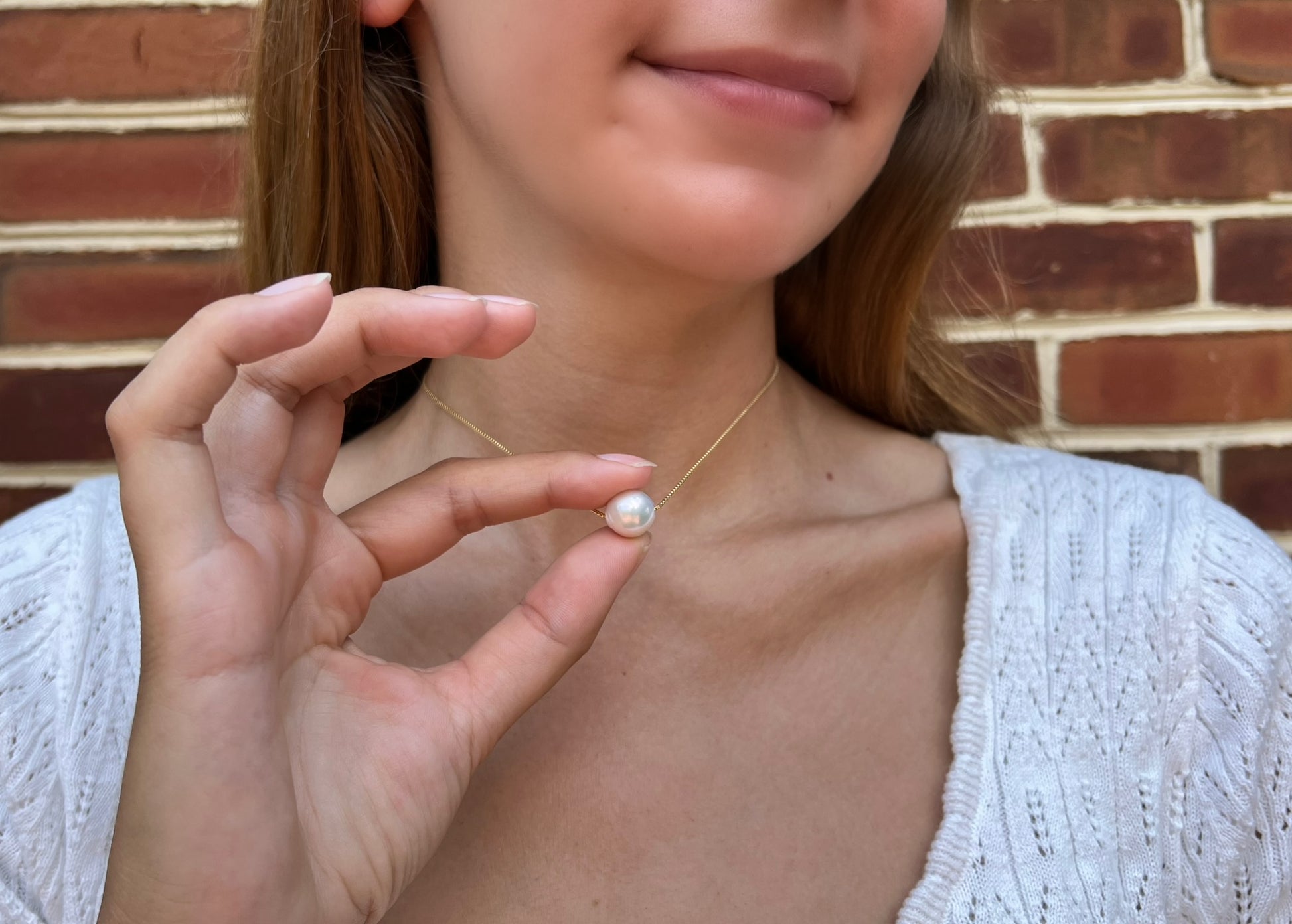 model holding up large pearl necklace which moves on the chain