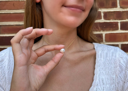 model holding up large pearl necklace which moves on the chain