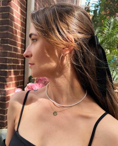 model wearing pearl strand necklace layered with engraved gold disc necklace