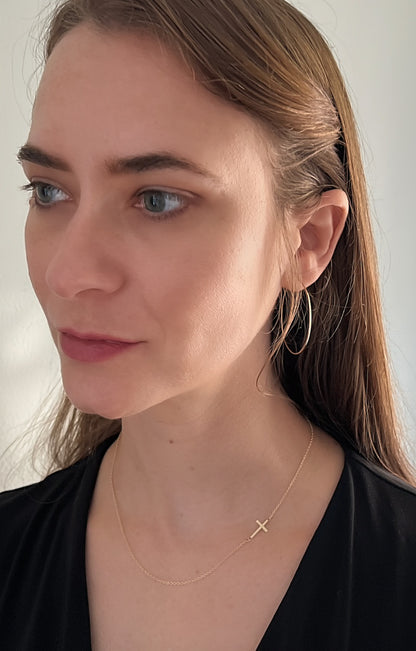 model wearing sideways cross necklace with thin gold hoop earrings