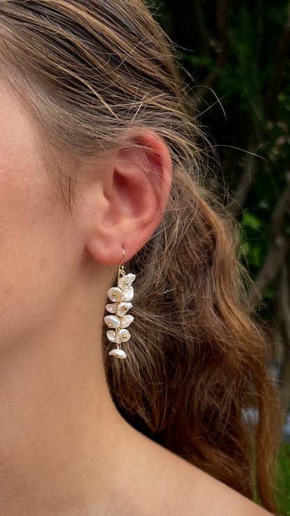 close up of model wearing keshi pearl earrings.  Off white pearls resembling flower petals dangling from gold ear wires