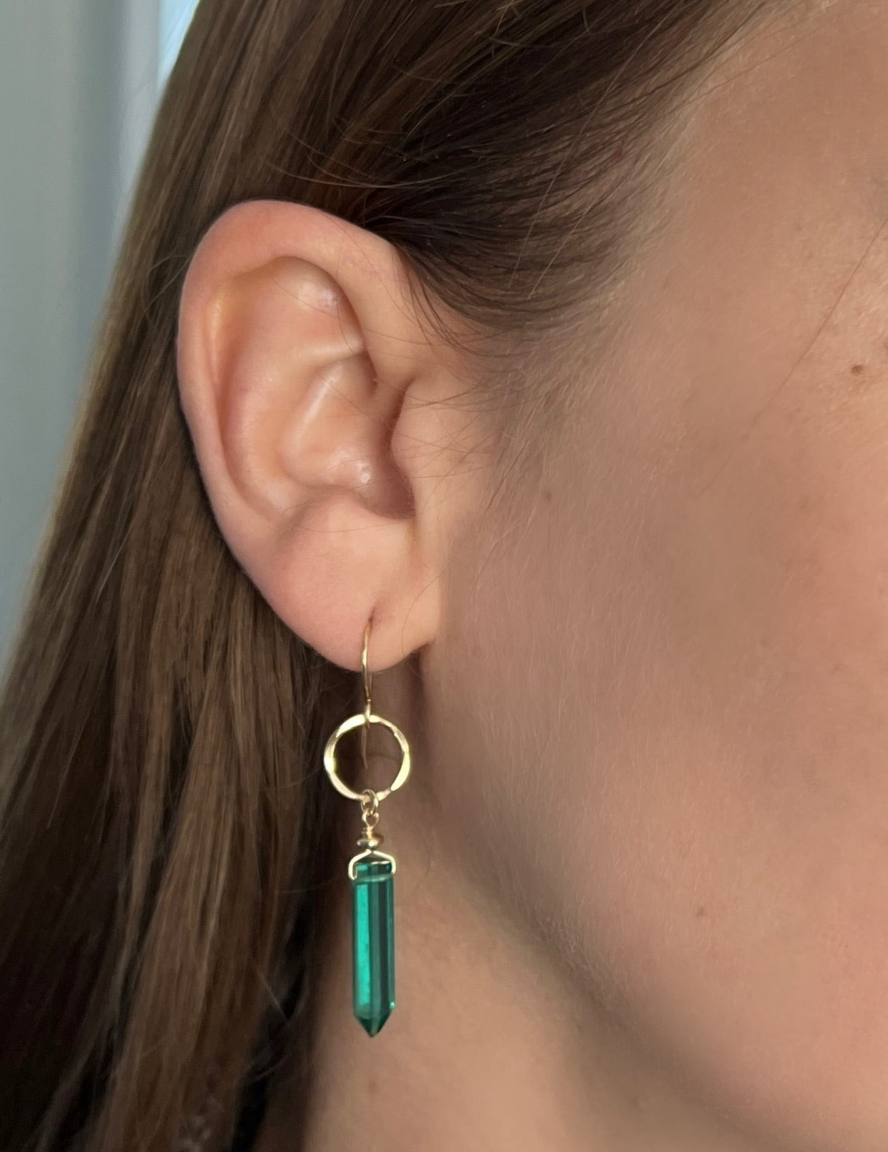 Close-up of an ear wearing a gold earring with a green gemstone.