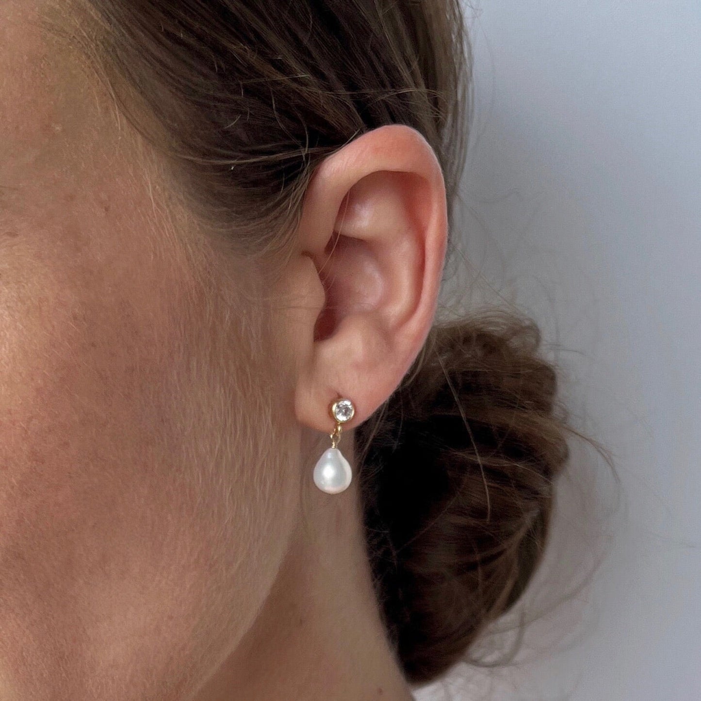 close up of model wearing Vivara Baroque Pearl Stud Earrings with cubic zirconia post earrings and a dangling pearl
