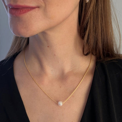 model wearing single pearl necklace floating on gold chain