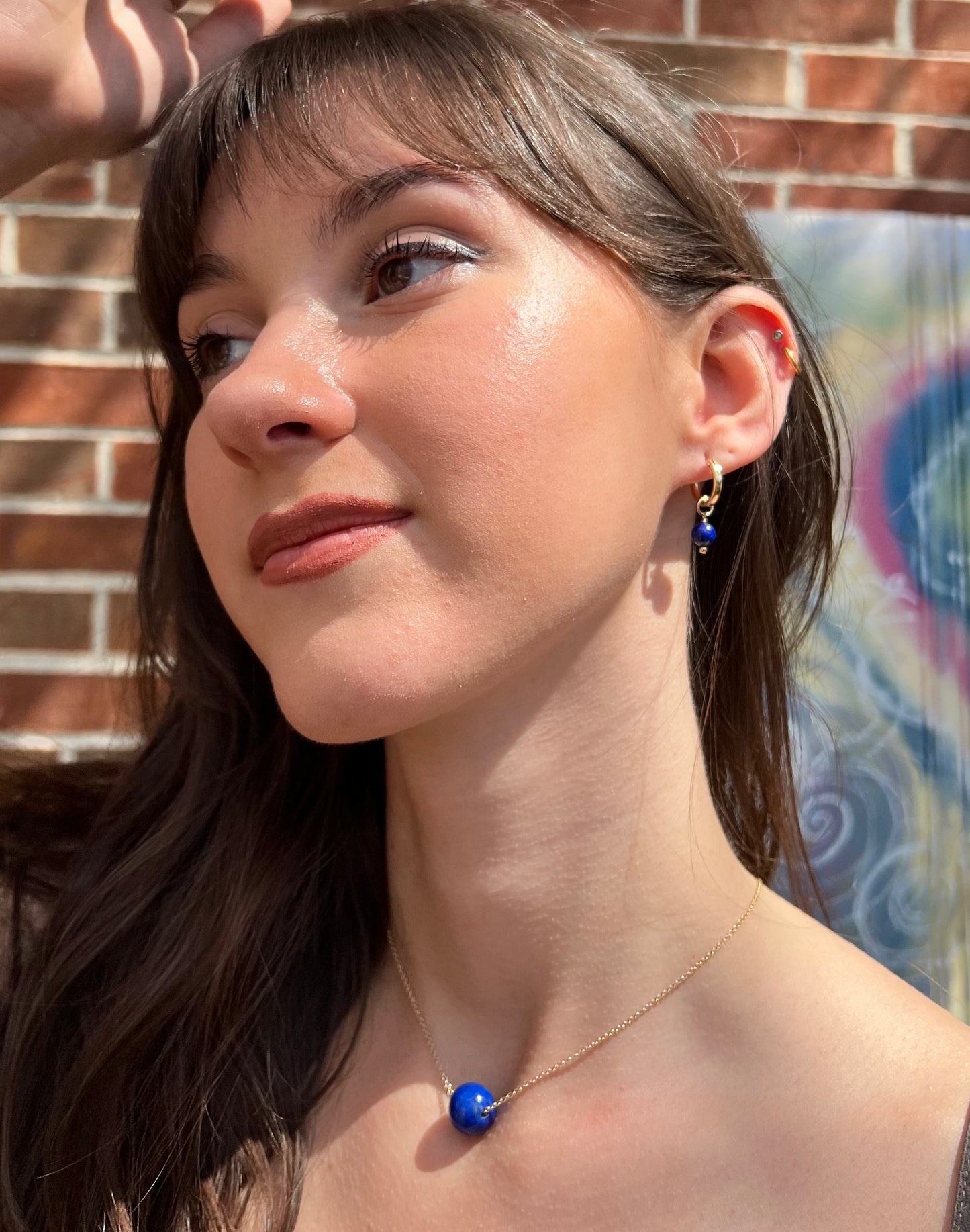 model wearing small lapis huggie earrings and large lapis ball necklace