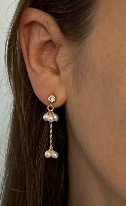 Close-up of an ear wearing a pearl earring with a gold chain.