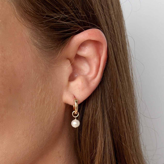 close up of model wearing Lucia pearl huggie earrings in 14k gold filled
