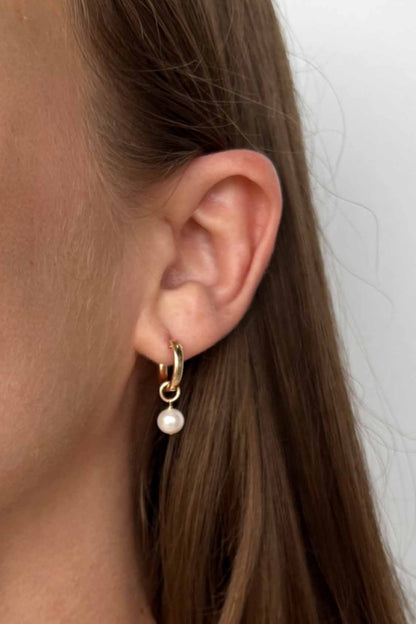 close up of model wearing gold filled huggie earrings with pearl dangle