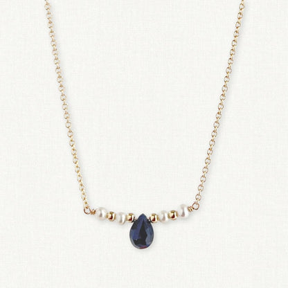 close up of tiny pearl bar necklace with small natural sapphire in the center on gold chain necklace