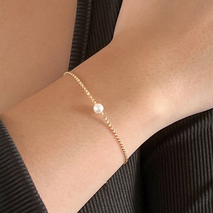 Gold chain bracelet with a single tiny akoya pearl shown on a wrist