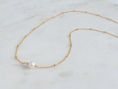 Gold necklace with a single pearl on a light marble background