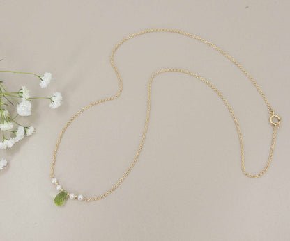 full photo of necklace showing gold chain with small peridot gem in the center surrounded by tiny pearls