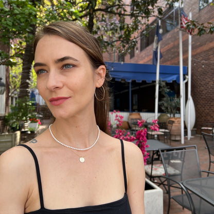model wearing classic gold hoop earrings and two layered necklaces including a white pearl strand
