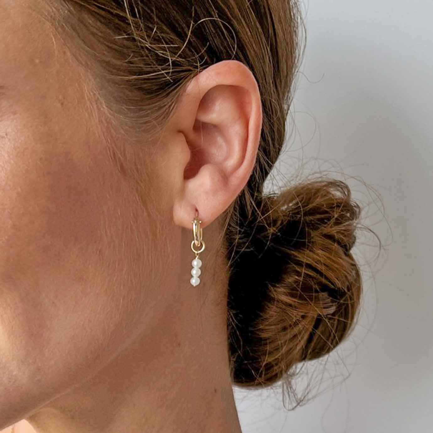 close up of model wearing huggie hoops with tiny pearl dangles shown in gold