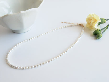 Pearl necklace on a white surface with a small flower and ceramic dish.