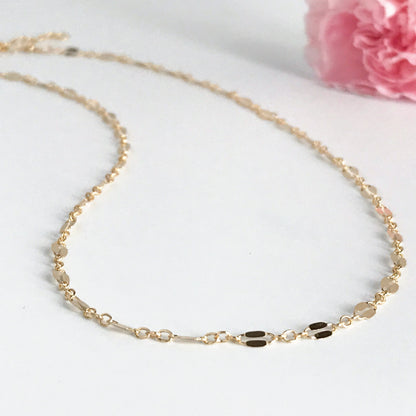 A gold-filled choker necklace with an adjustable length, featuring a shiny flat 'lacy' pattern.